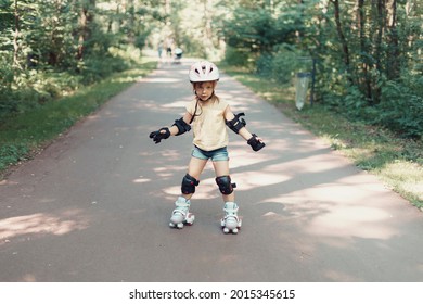 Baby In Protective Sportswear. Little Girl Is Rollerblading In The Park.