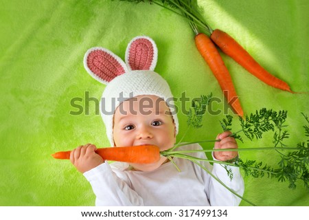 Baby in rabbit hat eating fresh carrot