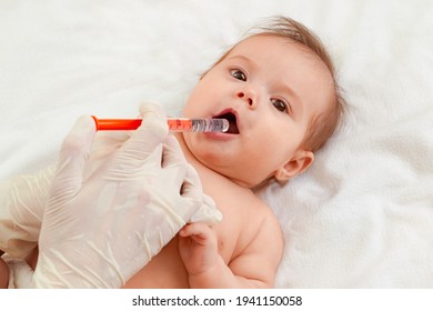 Baby receives medicinal syrup in his mouth with a syringe.