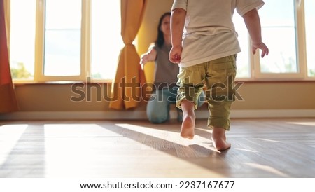 baby runs to mom at home. a child with bare legs runs across the floor to his mother against a sunny window. happy family kid dream concept. kid running back view at home hugging lifestyle mom