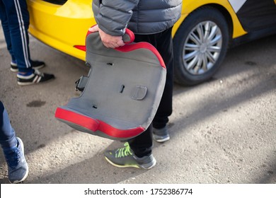 Baby Safety Seat For Car. A Man Gets In A Taxi. Preparing Guy Is A Special Seat For A Child. The Car Pulled Up For Passengers.