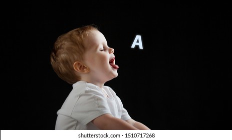 Baby Says, The Concept Of Problems With Dyslexia And Dysgraphia. A Child Learns To Speak, A Boy On A Black Background, A Letter A On The Right