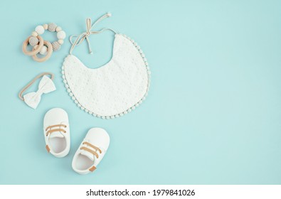 Baby Shoes, Bib And Teether On Blue Background. Organic Newborn Accessories, Branding, Small Business Idea. Baby Shower Invitation, Greeting Card. Flat Lay, Top View