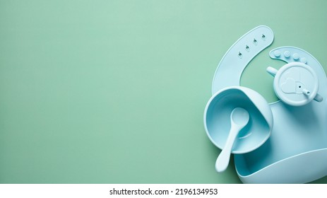 Baby Silicone Feeding Set. Flat Lay Baby Sippy Cup, Bib, Bowl With Spoon On Pastel Green Background. Top View.