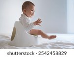 A baby sits on a potty training seat with a calm and focused expression, holding a baby toy.  Perfect for themes related to baby care, parenting, potty training, and early childhood development.