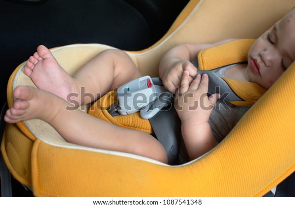 Baby sits in the orange car seat, red spot on his\
forehead and arm 