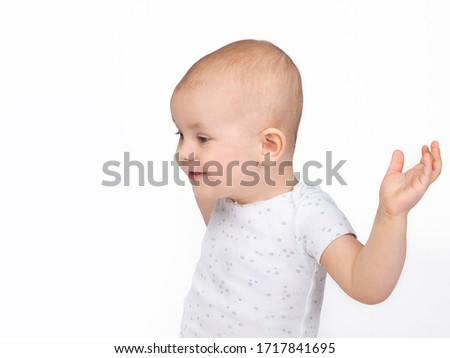 The baby sits sideways and looks at the object in surprise, raising his hands up. Surprise. Side view. Funny children's emotions.