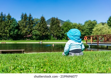 A Baby Sits With Sun Protective Clothing At A Lake In Summer