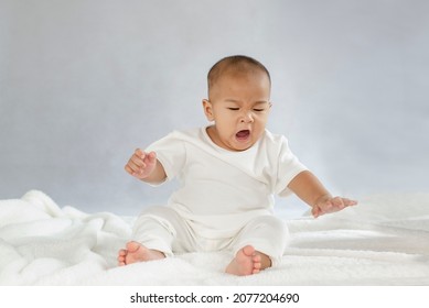 Baby sits yawning on a white mattress.