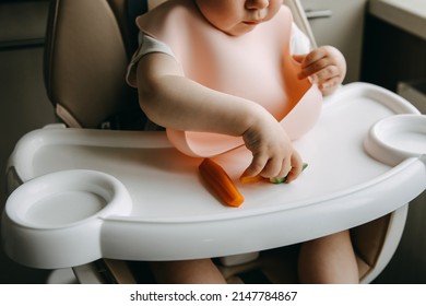 Baby sitting in high chair, with a silicone bib, eating vegetables. - Shutterstock ID 2147784867
