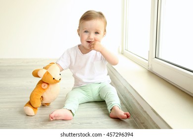 Baby sitting with teddy bear at window in room