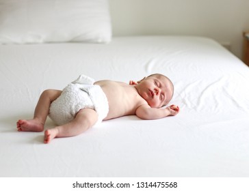 Baby Sleeping On Bed With White Sheets Wearing Cloth Diaper Nappy In Natural Light 