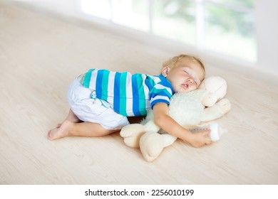 Baby sleeping on wooden floor with large window with stuffed toy sheep and milk formula bottle. Warm underfloor heating and windows isolation. Funny little boy falling asleep after crawling at home.  - Powered by Shutterstock