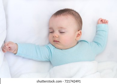 Baby Sleeping With Open Arms And Whihtout Pacifier In A Cradle. Light Blue Pajama And White Bed Sheets. 