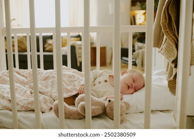 Baby sleeping peacefully in a crib, snuggling with a teddy bear, in a cozy room with natural light casting a soft glow - Powered by Shutterstock