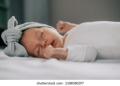 The baby sleeps on a white sheet, fell asleep with a bow on her head. newborn girl
