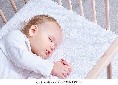 The baby sleeps safely and sweetly in his wooden crib on a terry sheet with an elastic band. Infant sleeping in bedside bassinet. Safe co-sleeping in bed side cot. Little girl taking a nap. Copy space - Shutterstock ID 1939193473