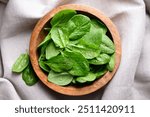 Baby spinach leaves with water drops in a wooden bowl on linen tablecloth. Raw organic spinach greens close up