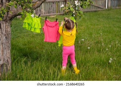 A baby is standing with back to a clothesline with bright colored wet children's clothes drying in the wind