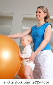 A Baby Standing At Physiotherapy Beside A Fitness Ball