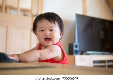A Baby Standing Up In The Red Tank Top