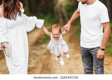 Baby swings holding hands of parents. Summer family walk. - Shutterstock ID 2269341765