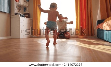 baby takes first steps close up. happy family kid dream concept. baby son takes first steps on the floor father helps son teaches him to walk. baby first steps close-up indoors lifestyle