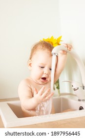 Baby Taking Bath In Kitchen Sink. Little Boy Bathing. Water Fun For Kids. Hygiene And Skin Care For Children. A Bouquet Of Sunflowers Stands Nearby