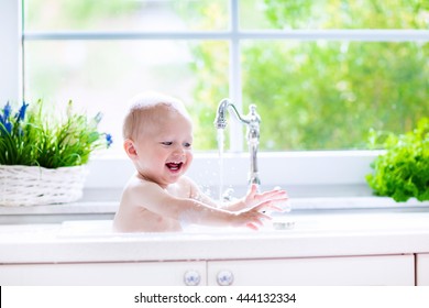 Baby Taking Bath In Kitchen Sink. Child Playing With Foam And Soap Bubbles In Sunny Bathroom With Window. Little Boy Bathing. Water Fun For Kids. Hygiene And Skin Care For Children. Bath Room Interior