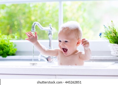 Baby Taking Bath In Kitchen Sink. Child Playing With Foam And Soap Bubbles In Sunny Bathroom With Window. Little Boy Bathing. Water Fun For Kids. Hygiene And Skin Care For Children. Bath Room Interior