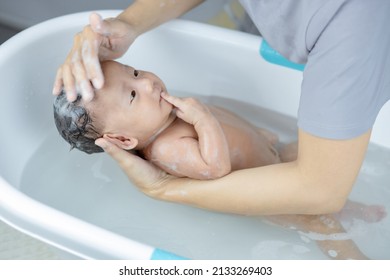 baby taking bath, mother hands supporting his head.