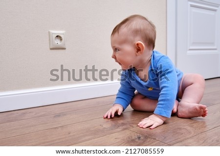 Baby toddler is near the electrical outlet on the home wall. Danger and protection of child fingers from electric shock, aged 6-11 months