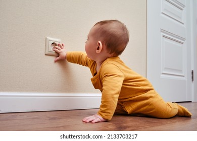 Baby toddler reaches into the electrical outlet on the home wall with his hand. Danger and protection of child fingers from electric shock, aged 6-11 months