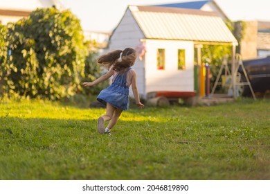 Baby Toddler Running On Green Lawn Near The House.