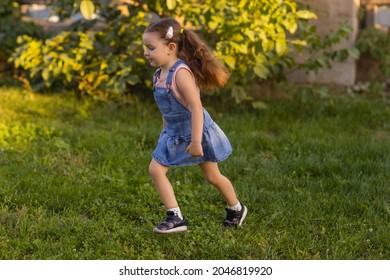 Baby Toddler Running On Green Lawn Near The House.