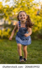 Baby Toddler Running On Green Lawn Near The House.