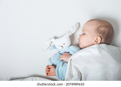 Baby with toy in hands sleeps on bed. Infant development concept, toddler restful sleep, teething, colic.