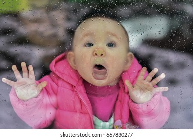 Baby Trying To Lick Rain Drops On The Window's Glass Outside, Pressing Face Against  The Glass