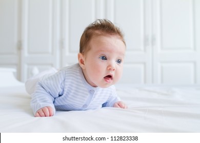 Baby tummy time, wearing blue clothes in a white nursery