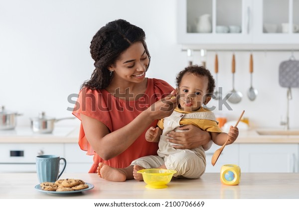 Baby Weaning. Caring Black Mother Feeding Little\
Toddler Son From Spoon In Kitchen, Loving African American Mommy\
Giving Porridge Or Mash Fruit Puree To Cute Little Child At Home,\
Closeup Shot