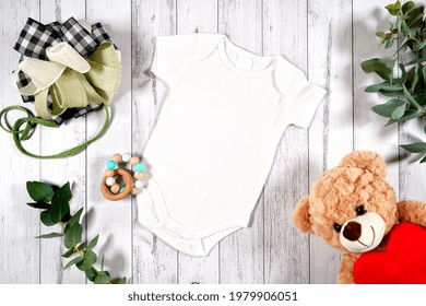 Baby wear romper onesie flatlay. On-trend farmhouse theme craft product mockup with farmhouse style decor, on a white wood background. Negative copy space for your design here.