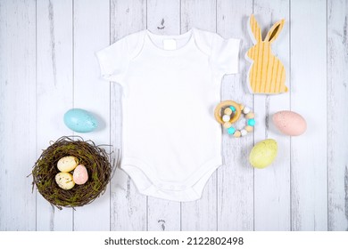 Baby wear romper onesie mockup. Happy Easter farmhouse theme SVG craft product mockup styled with wooden bunny and pastel Easter eggs against a white wood background.