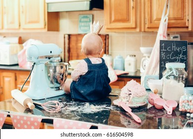 Baby Wearing Crown Sitting On A Messy Kitchen Counter With A Cake And A Mixer