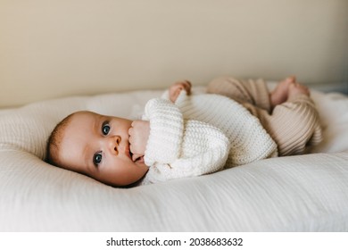 Baby wearing winter clothes, a warm knitted sweater and pants, sucking on her fist.