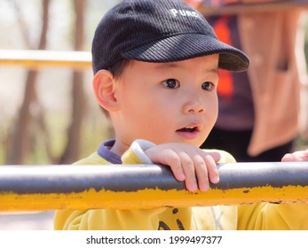 The Baby Is Wearing A Yellow Dress And A Black Hat, Playing On An Outdoor Sports Facility