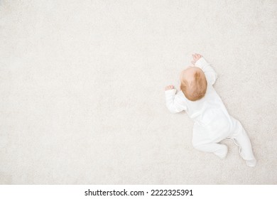 Baby in white bodysuit crawling on knee and arms on light beige home carpet background. Top view. 5 to 6 months old infant development. Empty place for text.