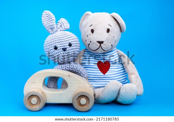 Baby wooden car toy, amigurumi in form of a\
rabbit and toy bear witn heart embroidered in striped clothes on\
blue background. Concept of baby toys.\
