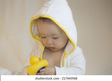 baby in yellow and white bathrobe playing with rubber duck