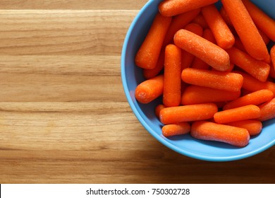 Baby-cut Carrots In Blue Bowl On Wood. Top Down View.