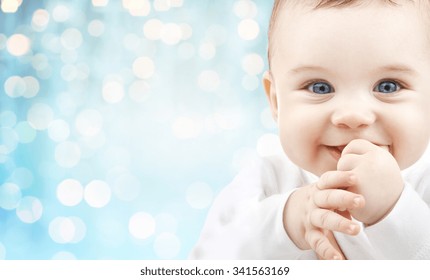 Babyhood, Childhood And People Concept - Happy Baby Face Over Blue Holidays Lights Background